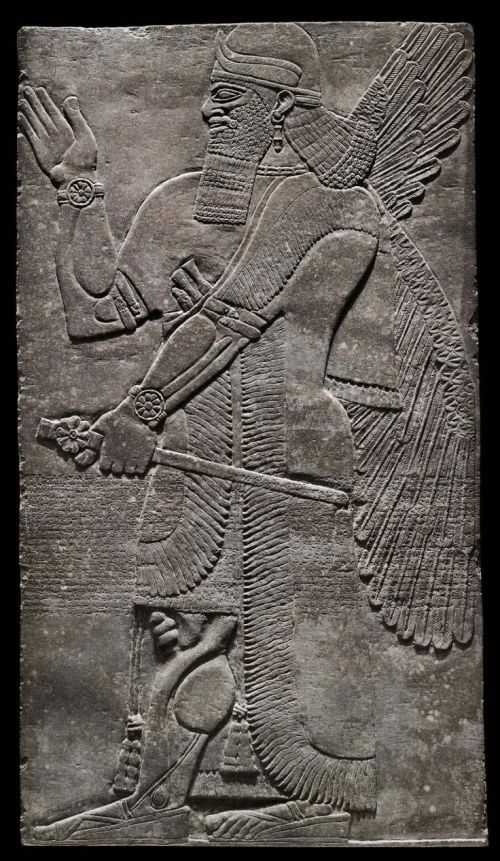 This umu-apkallū makes the iconic greeting gesture with his right hand while holding an e'ru stick in his left.  The tassels of his robe are clear around his ankles, as are bracelets just above his elbows.  Note the detail of the individually feathered wings. The rosette insignia on the e'ru and his wrist is not yet understood.  The headdress is a horned tiara, indicative of divinity. 